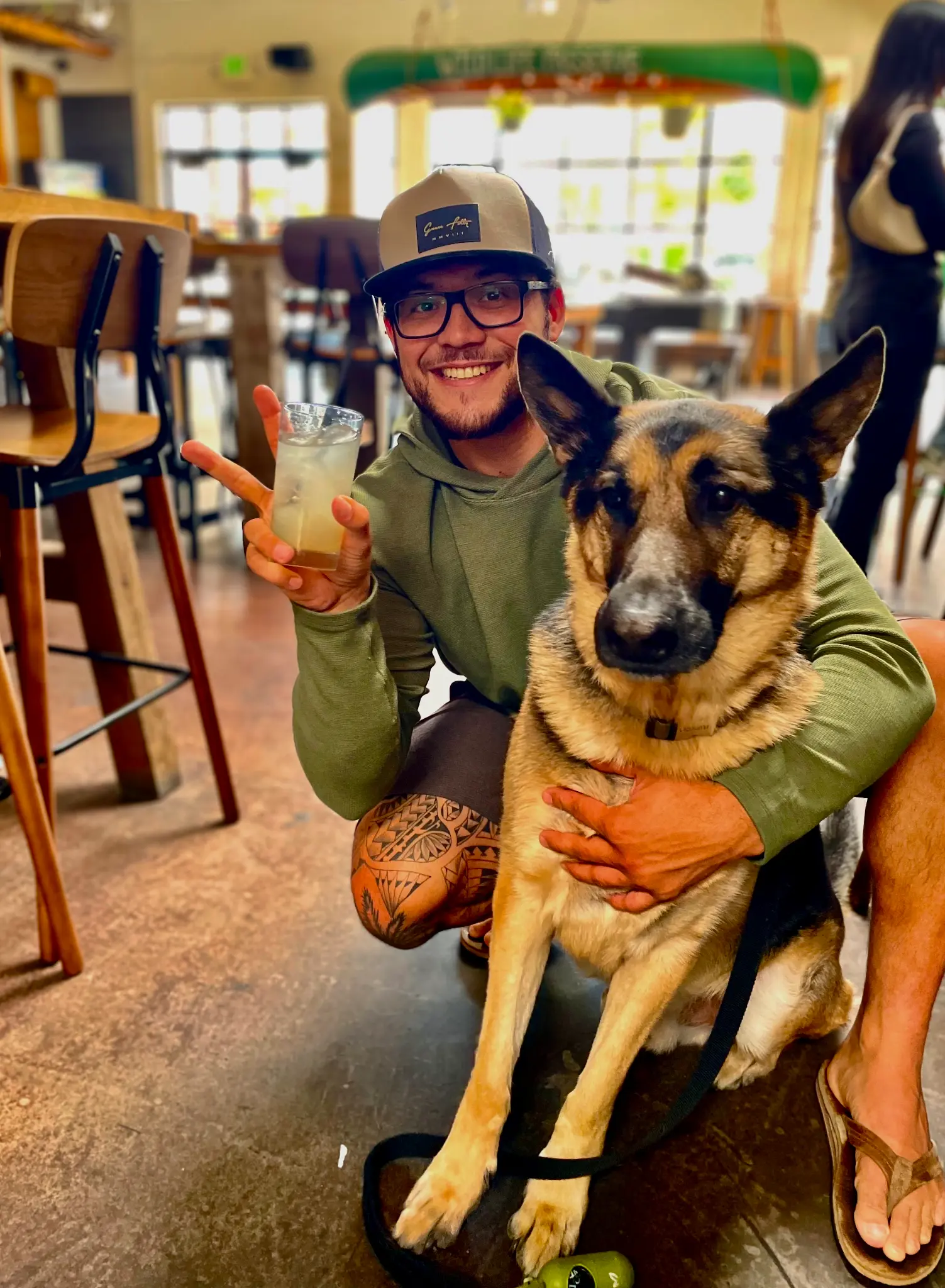Guest smiling and holding a cocktail with a peace sign while hugging a German Shepherd at Unbearable Skee Lodge