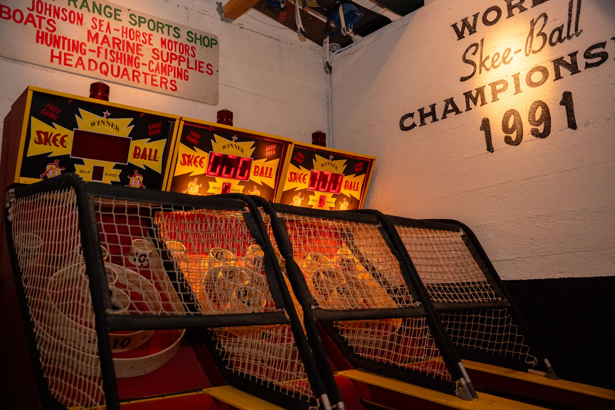 Three vintage Skee-Ball machines glowing at Unbearable Skee Lodge with the World Skee-Ball Champions 1991 mural painted on the wall